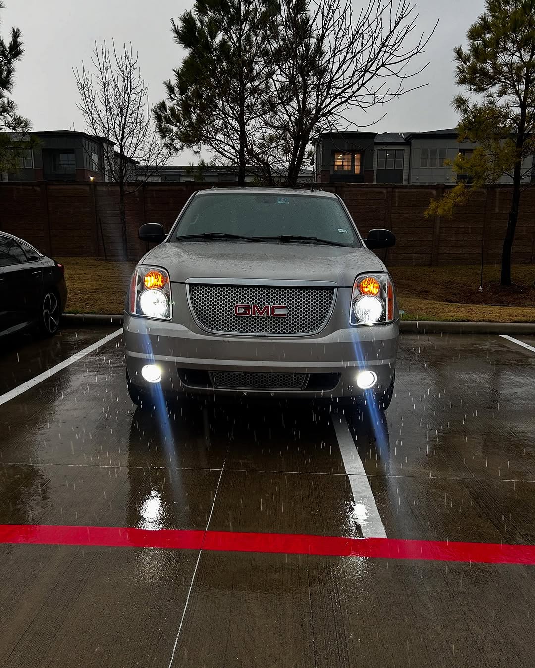 GMC Yukon Denali with headlights on during a rainy Houston evening